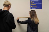 Two students measuring marks on a wall for class