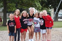 High school cheerleader posing with elementary students on playground