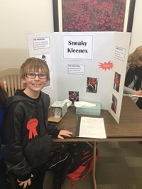 Elementary student standing near his invention, the Sneaky Kleenex