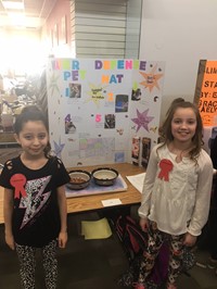 Elementary students standing near their invention, the Water Defense Pet Mat