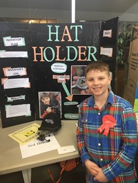 Elementary student standing near his invention, the Hat Holder