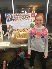Elementary student standing near her invention, the Squeaker Speaker Doggy Bed